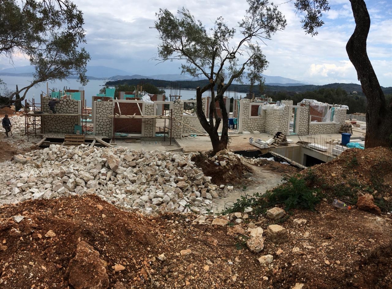 Wall sections part-clad in white stone behind piles of building stone, with the open sea beyond.