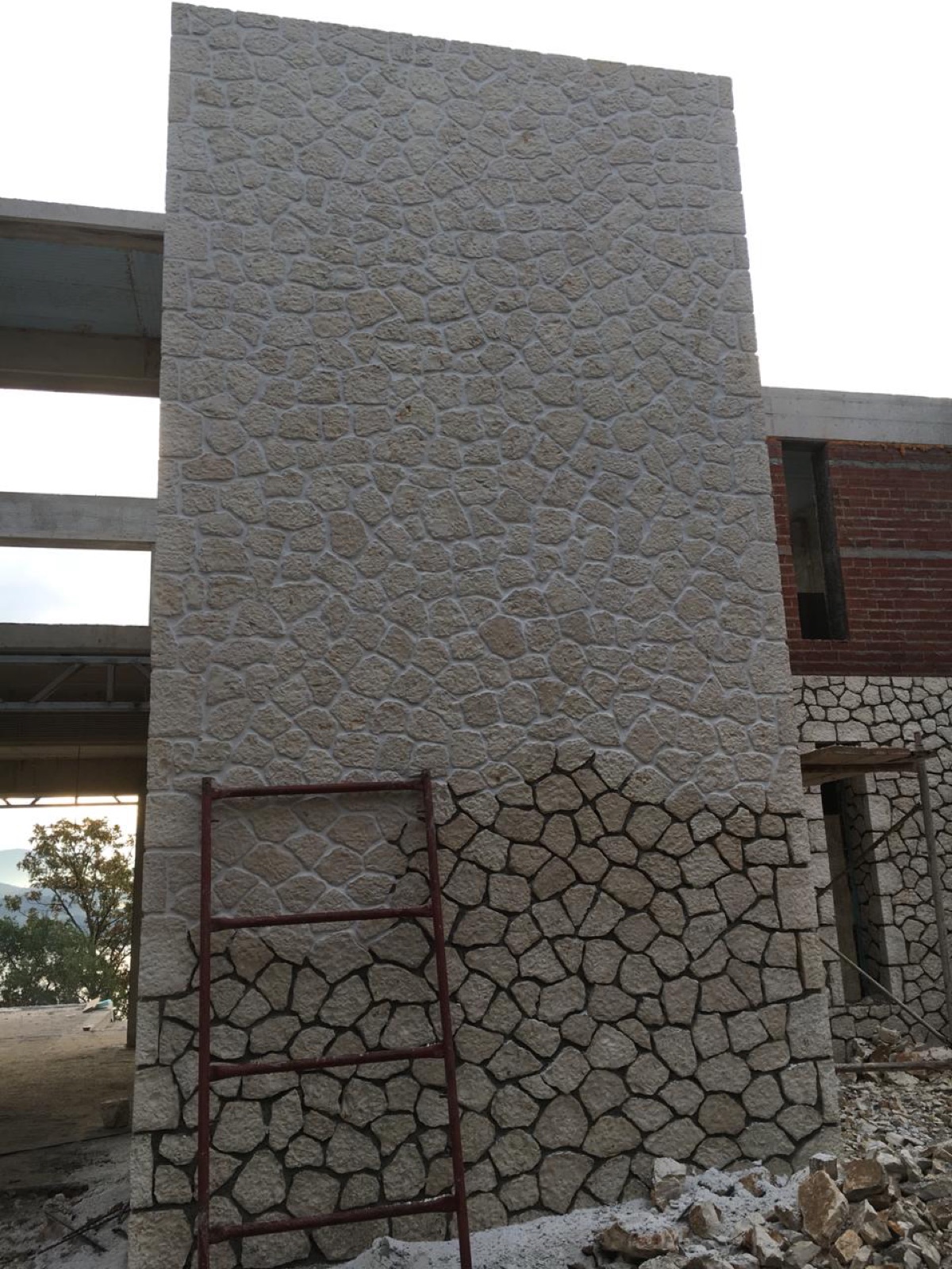 A tall pier half-clad in irregular cream limestone over its concrete frame, a red ladder resting against the wall.