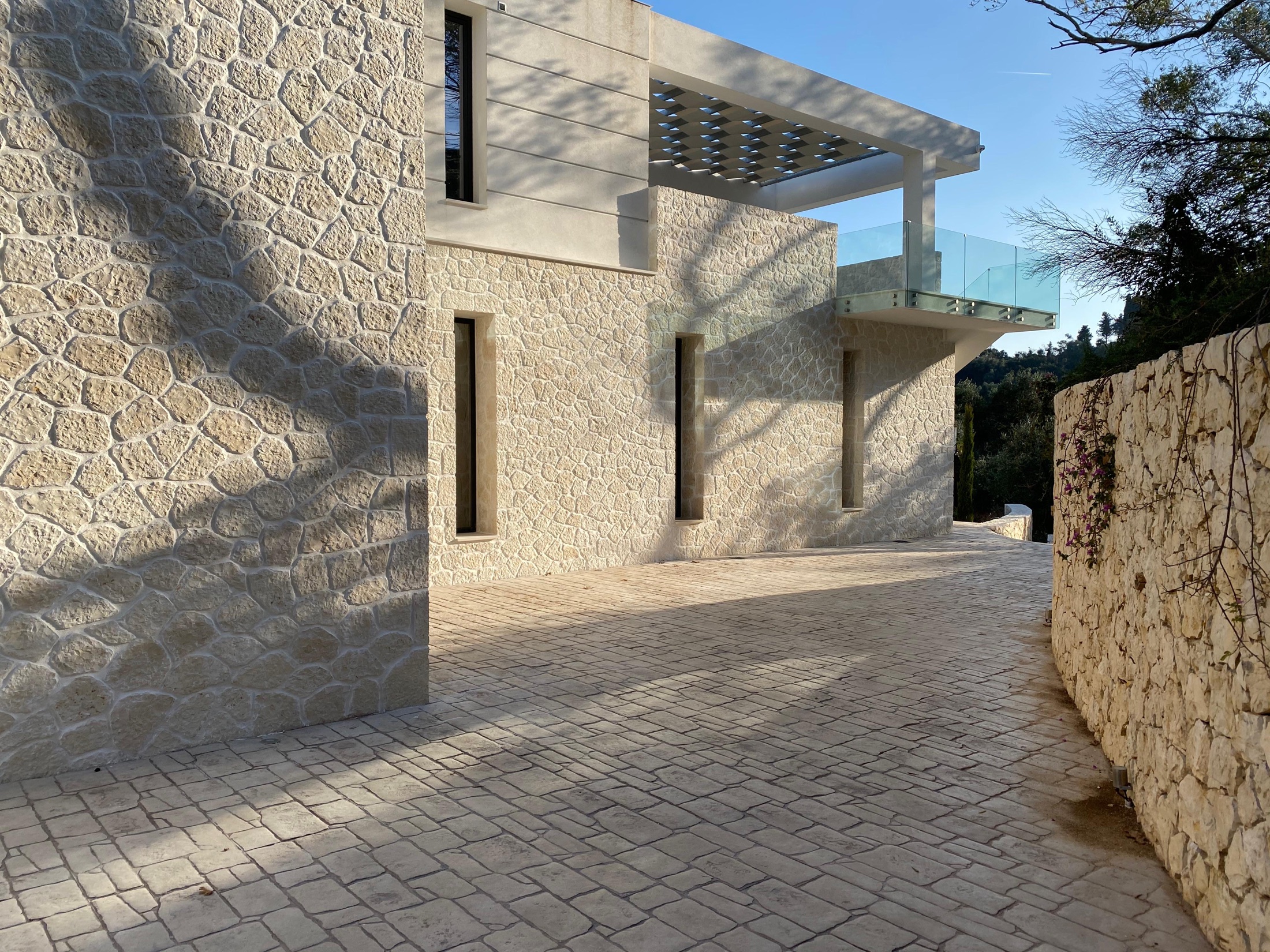 Hand-laid limestone villa walls and a cobbled stone drive on Corfu in low evening light.