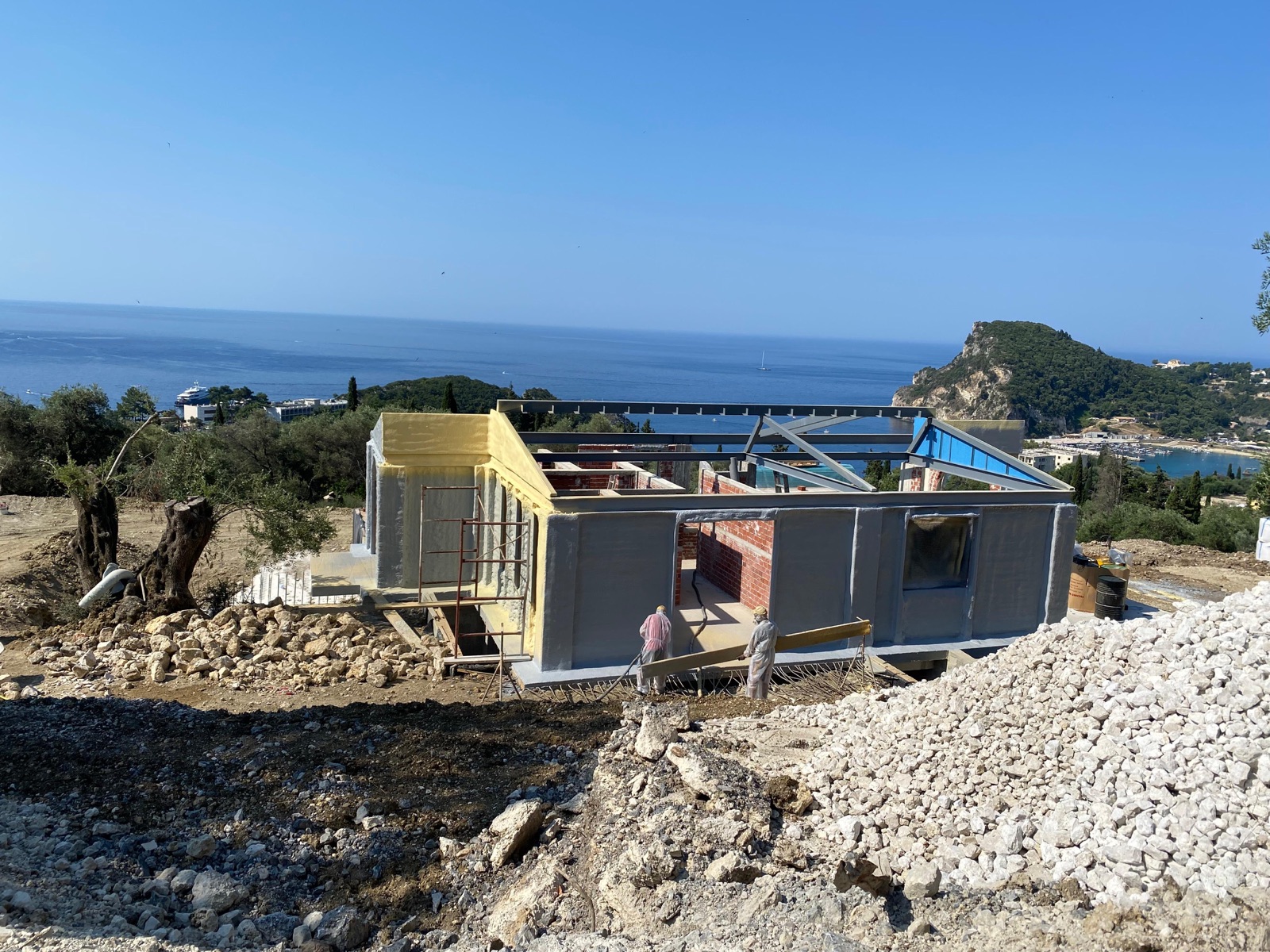 The insulated villa shell with steel roof framing, set against a sweeping view of blue sea, headland and bay.