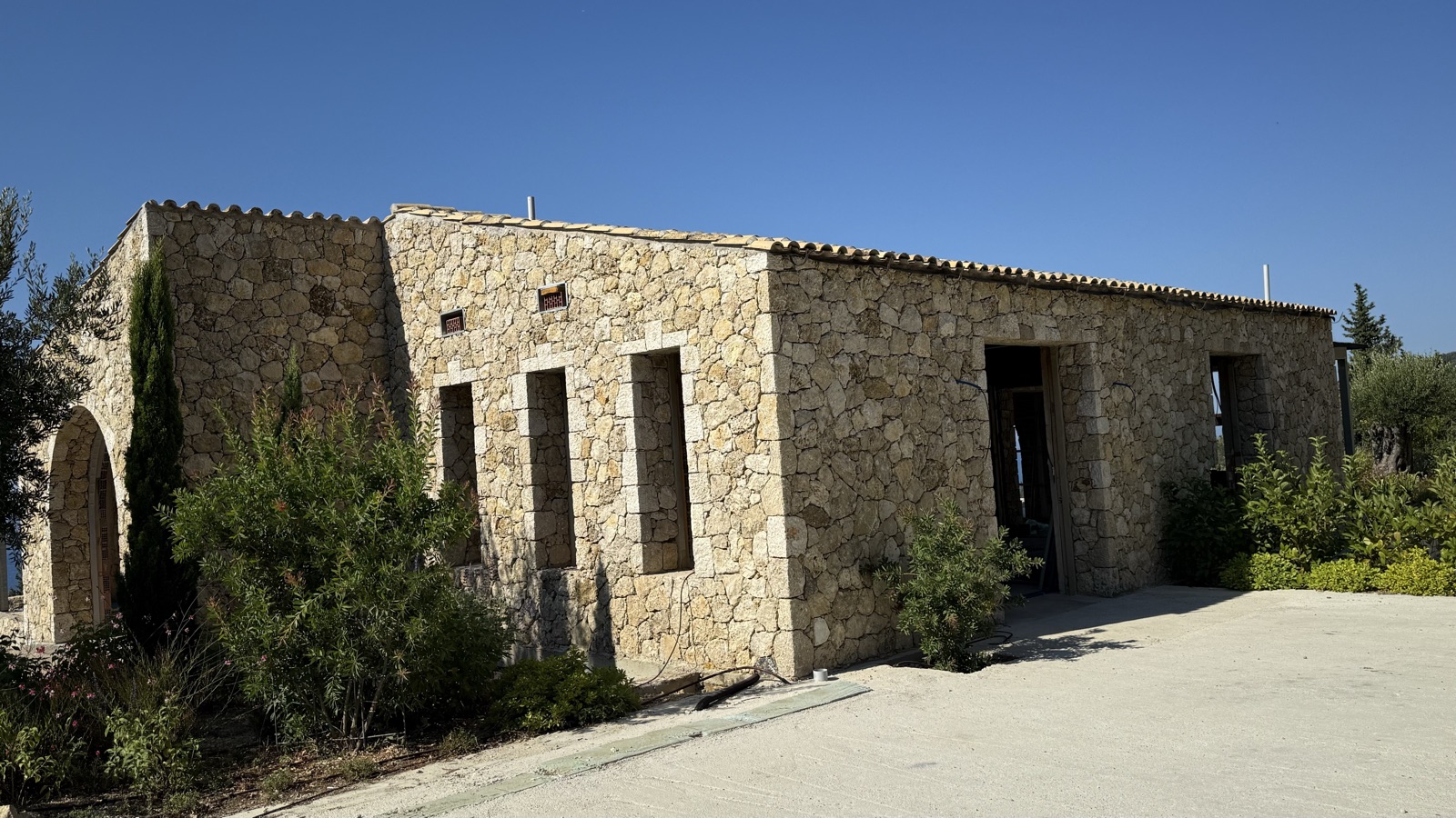Rough-cut honey limestone cladding in strong sunlight, with an arched opening and a terracotta dentil cornice along the roofline.