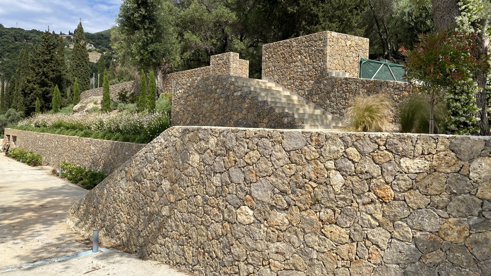 A battered stone wall corner with stepped caps, grasses softening the top and raking sunlight bringing out the rubble texture.