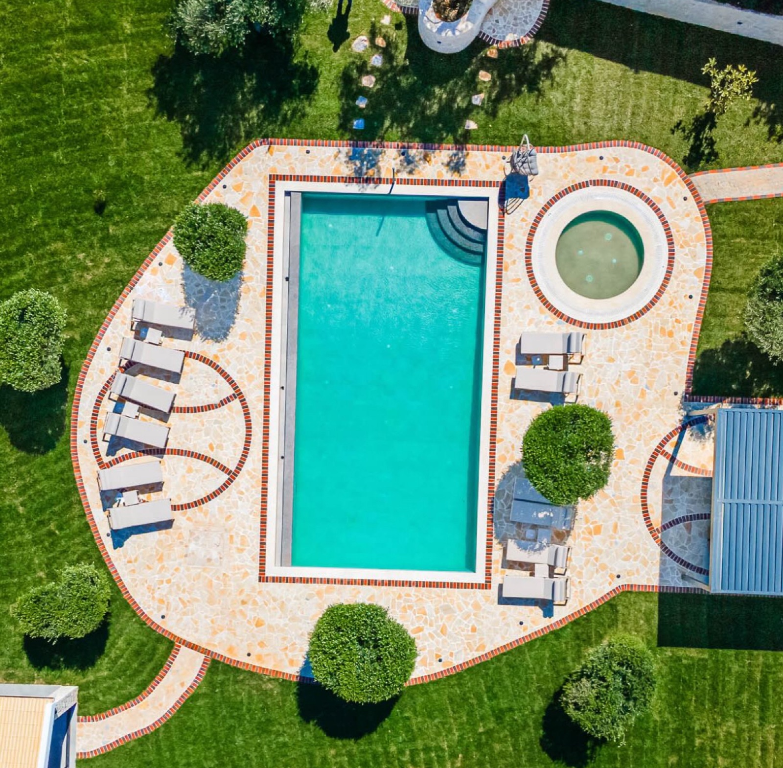 The rectangular turquoise pool and round spa from above, framed by terracotta brick borders and an ochre flagstone terrace.