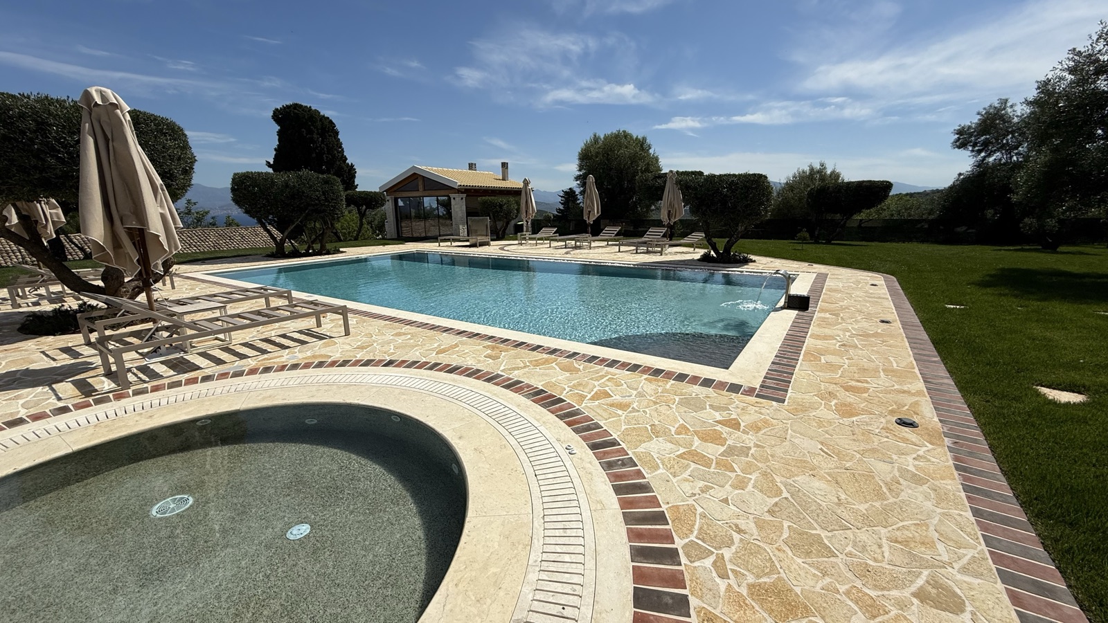 The round spa in the foreground and the infinity-edge pool beyond, ochre flagstone paving edged in terracotta brick.