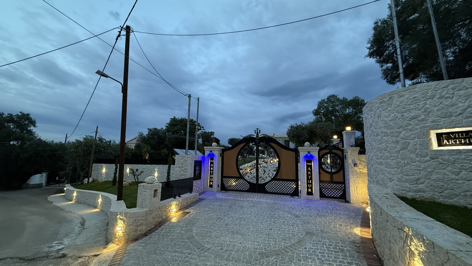The entrance walls and gates at dusk, warm uplighting grazing along the curved stone wall.
