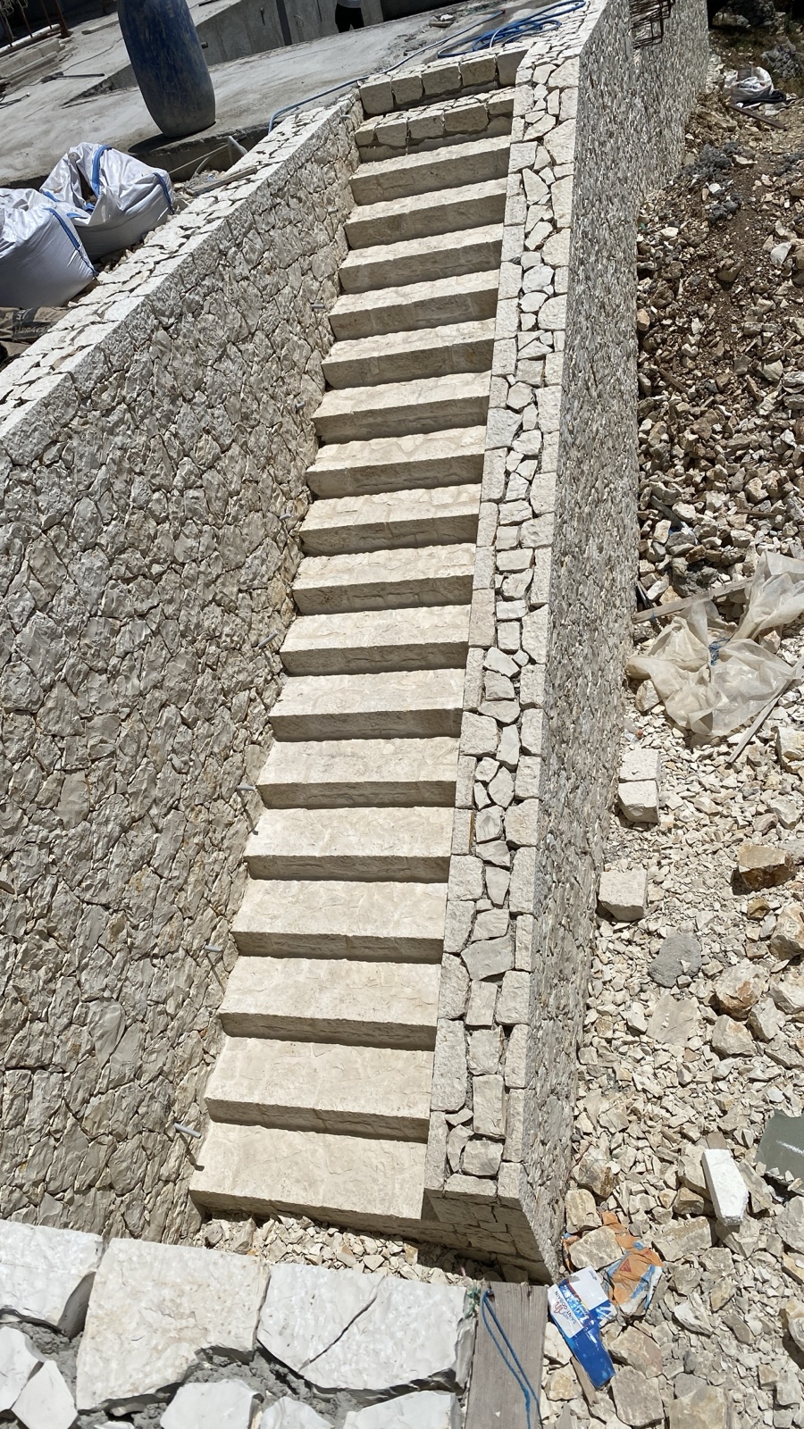The new stone staircase descending along a rough-faced cream limestone retaining wall, seen from above.