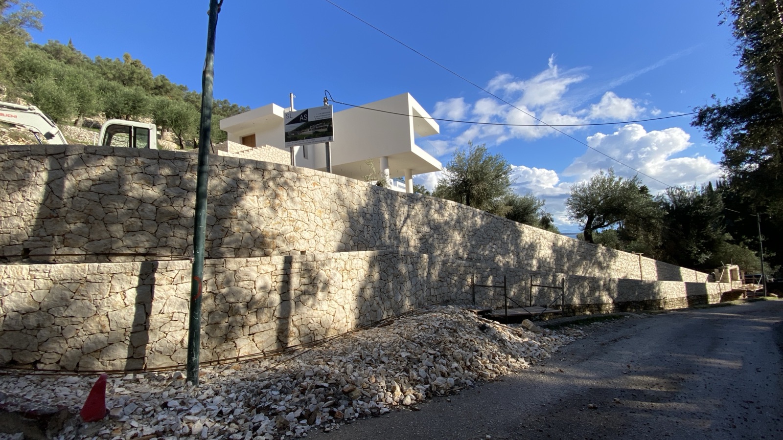 The long tiered limestone retaining wall running along the access road, the white villa rising above it.