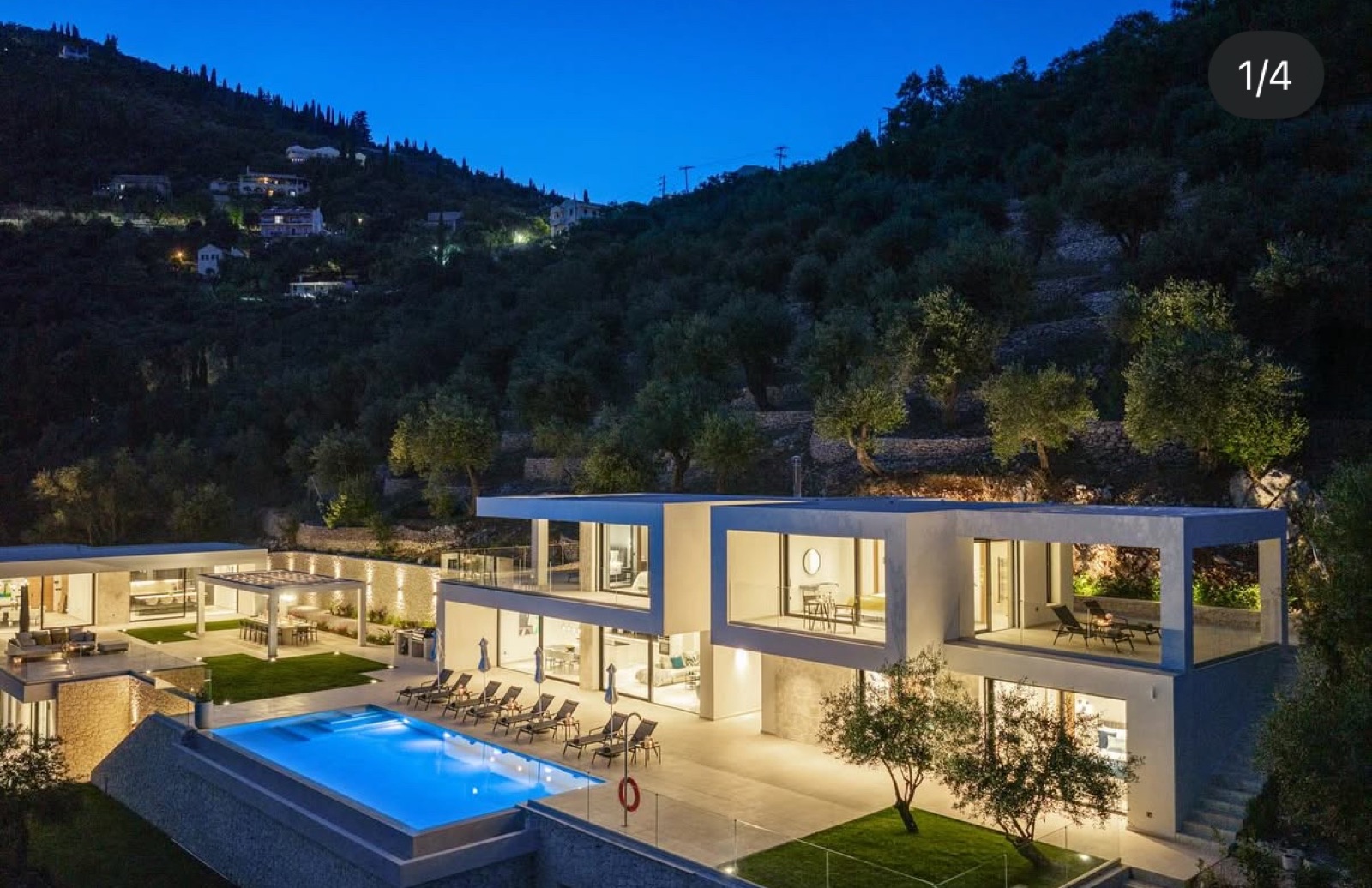 The illuminated villa and lit pool at night, seen from the garden side.