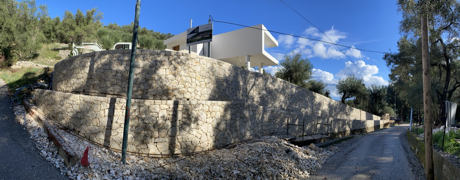 The curved stone retaining wall wrapping the road corner, the villa shell rising above it.