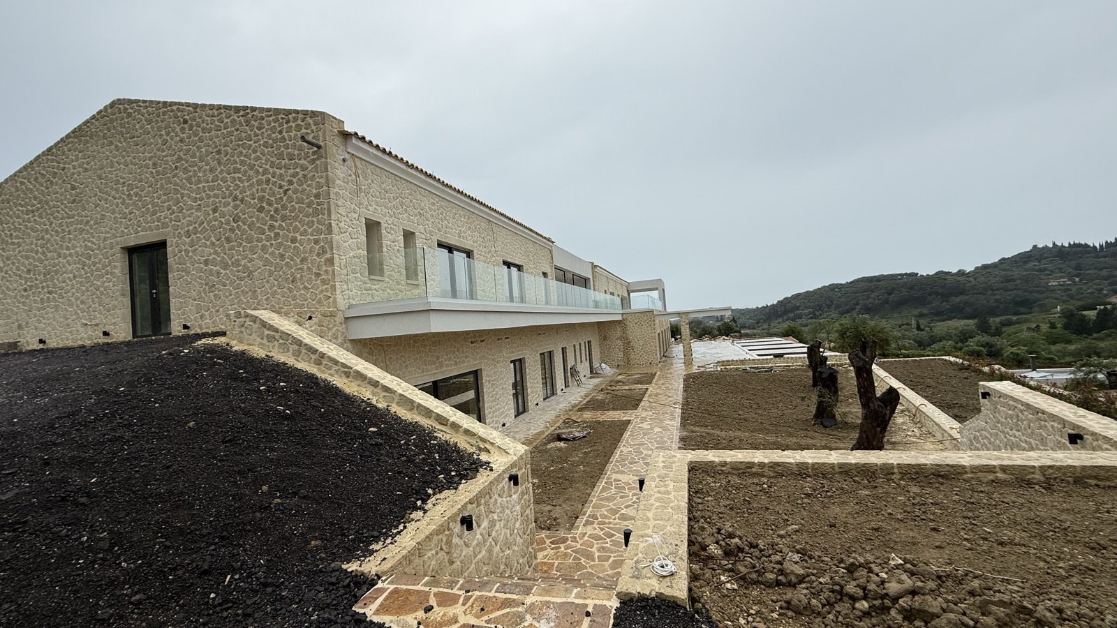 The upper level of the villa with its balcony, terraced stone planters holding olive trees and hills in the distance.
