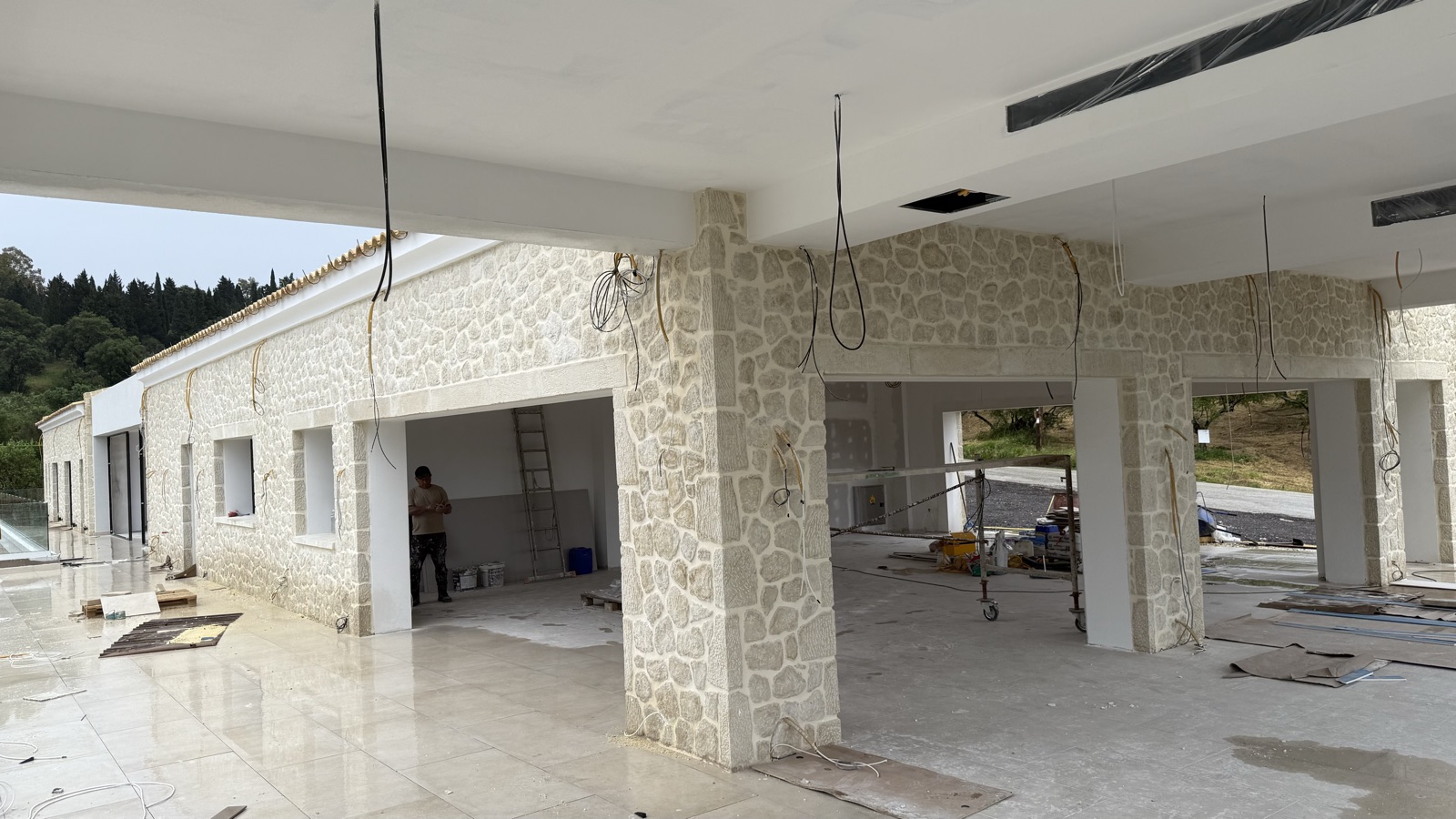 Stone-clad columns and walls inside the covered terrace, the floor polished and the ceiling still being fitted out.