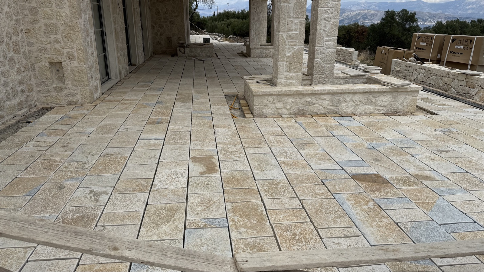 Freshly laid stone paving in cream, gold and blue-grey on the porch terrace, with stone pillars and a raised planter.