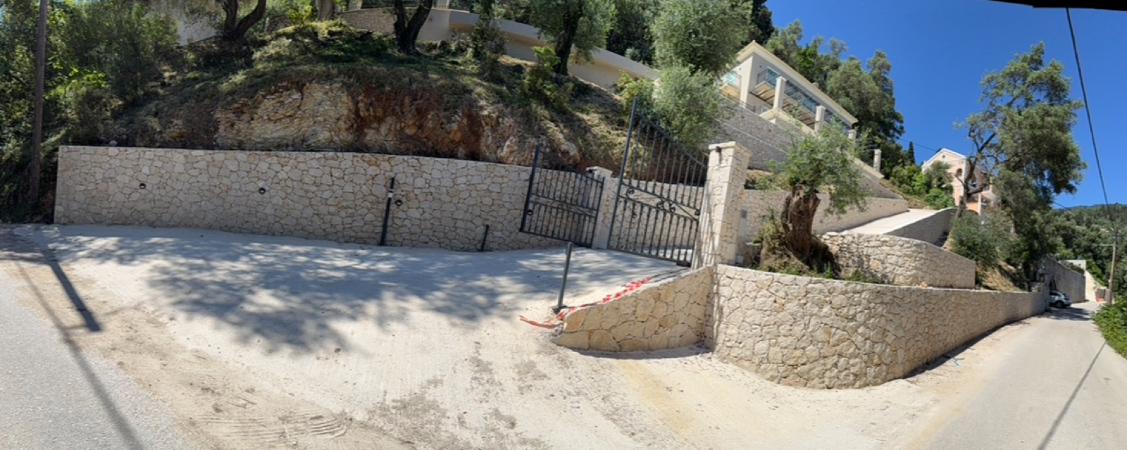 The full entrance sequence of iron gates, stone piers and sweeping retaining walls along the road, villa terraces above.